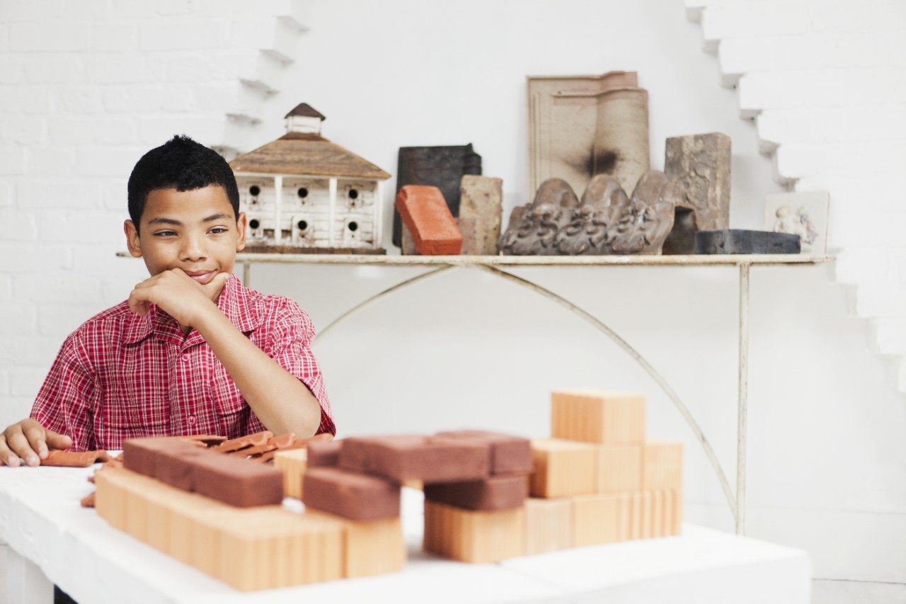 Thoughtful boy looking at stacked miniature bricks
