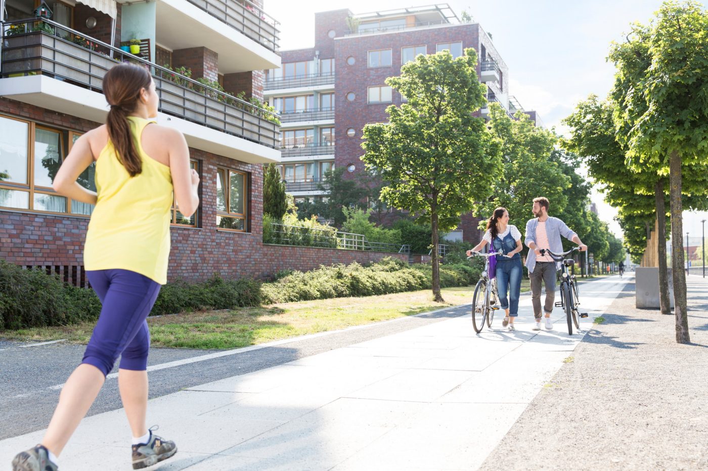 Couple pushing bicycles and woman jogging in a newly built housing estate