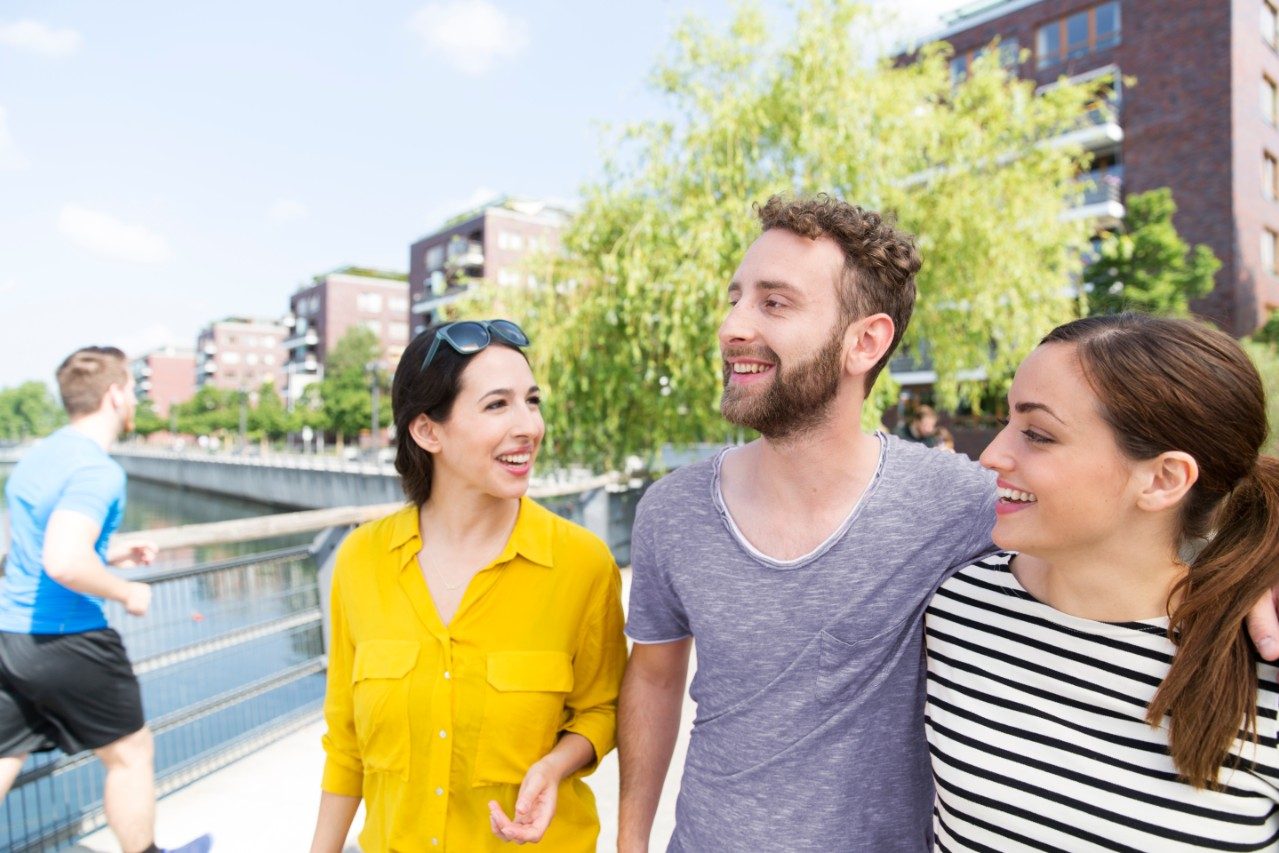 Besties time - Three friends walking along waterfront path next to newly built housing estate